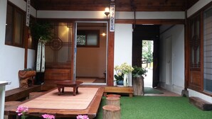 Un intérieur de style japonais traditionnel, avec un sol recouvert de tatamis, des meubles en bois et un petit espace jardin agrémenté d’une table et de bancs en bois.
