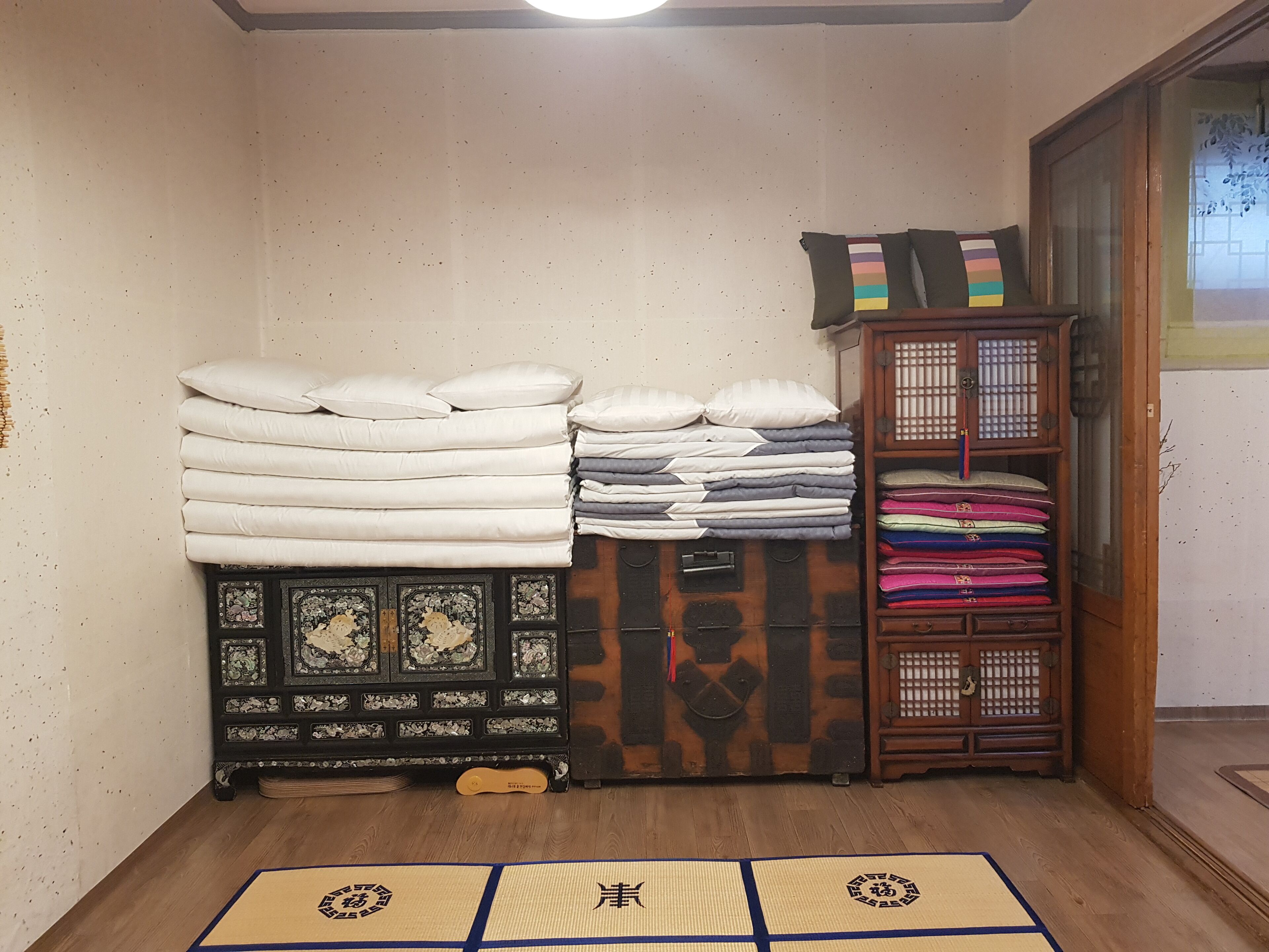 A room with a traditional Japanese tatami mat floor, a wooden cabinet with a decorative design, and a stack of folded bedding.