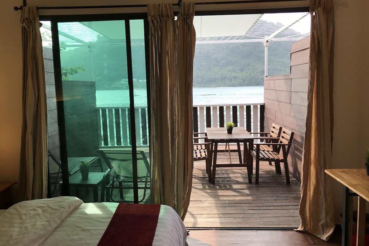 Une chambre avec un lit, un balcon doté d’une table et de chaises, et une vue sur une étendue d’eau.