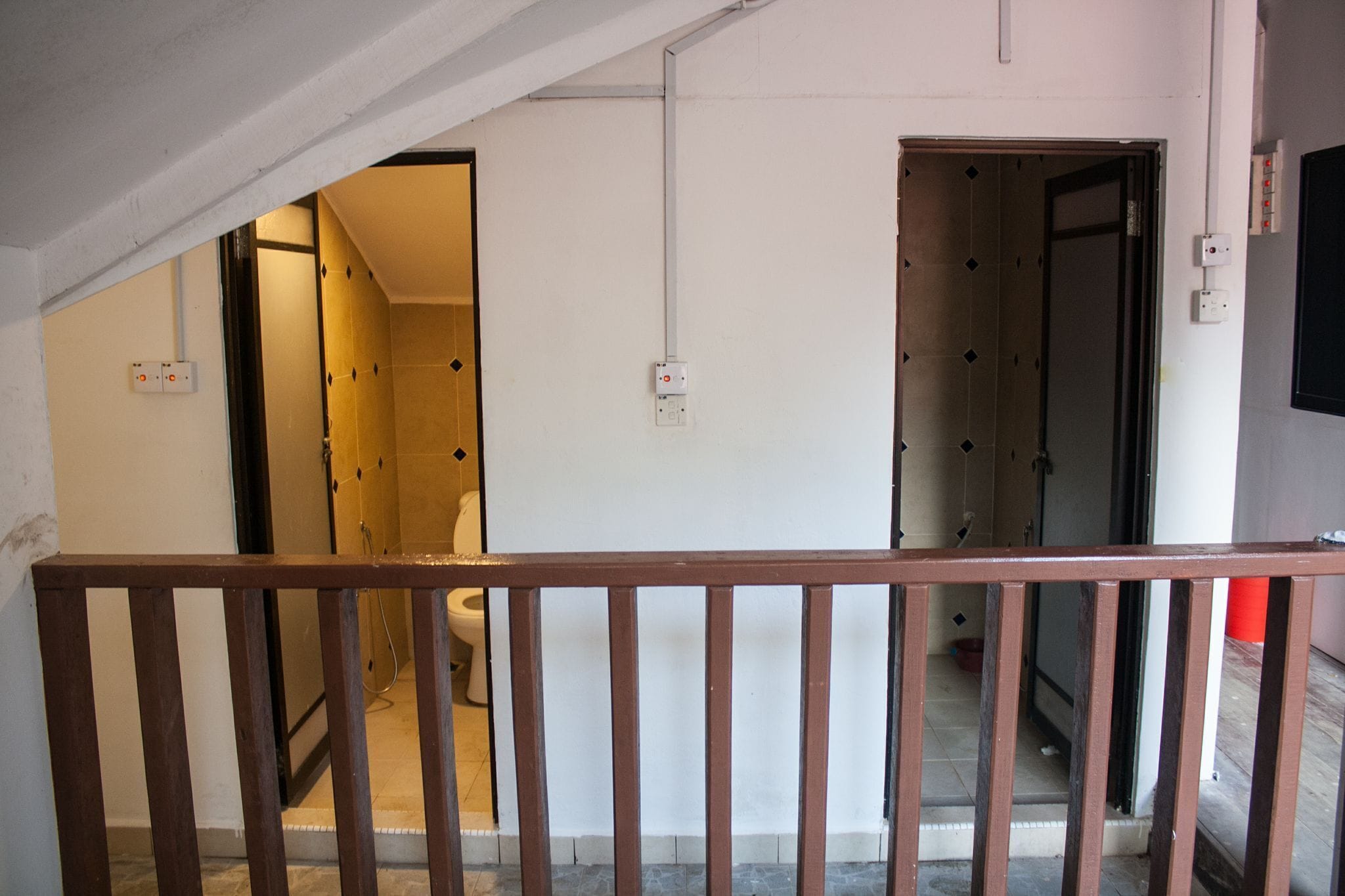 A staircase leading to a room with a toilet and shower, a wooden railing, and electrical outlets on the walls.