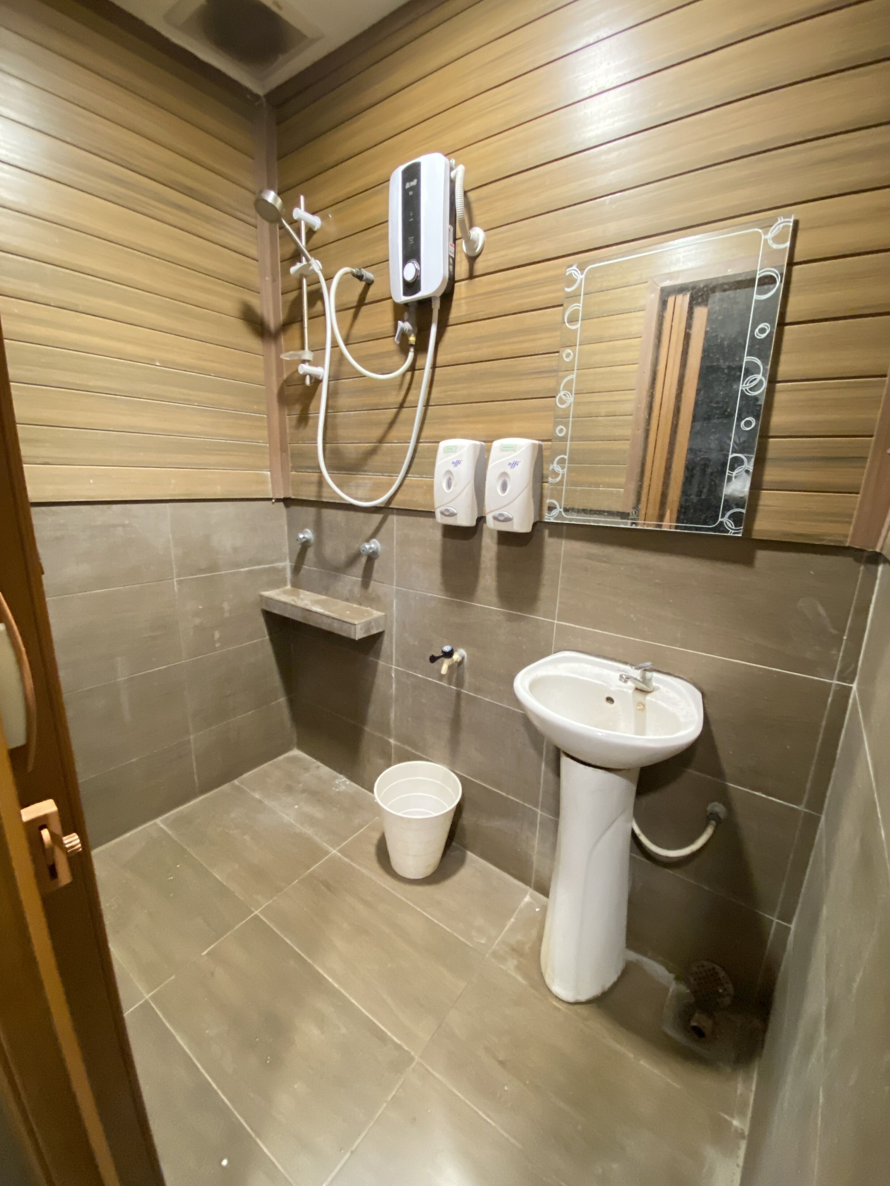 Un baño con pared de madera, un lavabo, un espejo y una ducha.