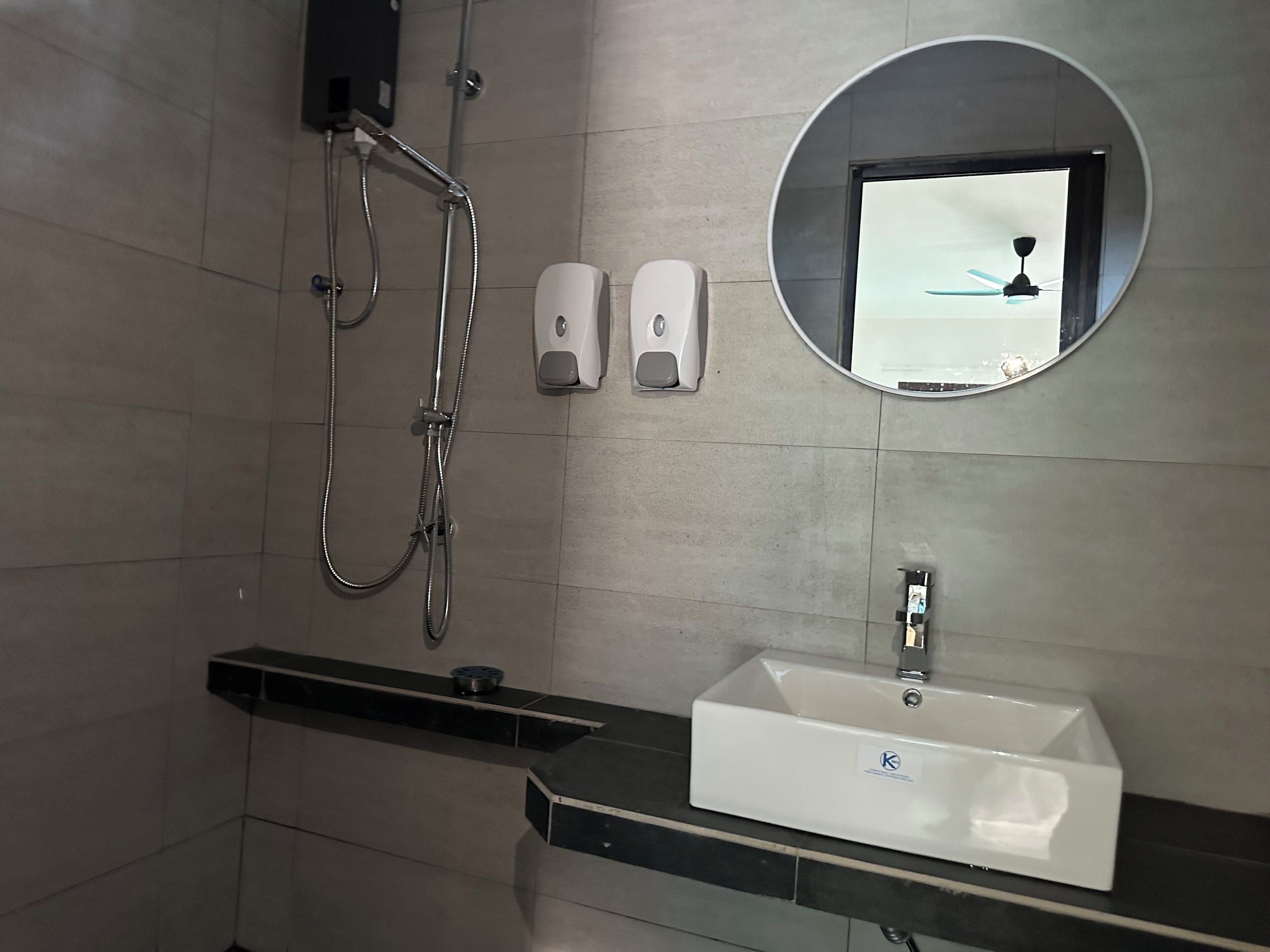 A modern bathroom with a rectangular sink, a handheld showerhead, and two soap dispensers mounted on the wall.