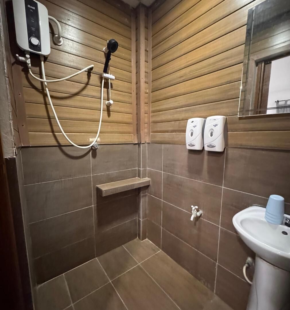 Een kleine, compacte badkamer met houten paneelwanden, een douche, een wastafel en twee zeepdispensers.