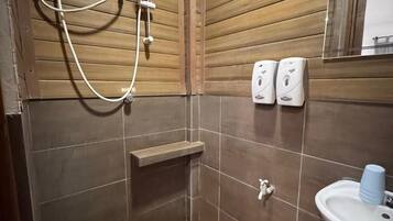 Een kleine, compacte badkamer met houten paneelwanden, een douche, een wastafel en twee zeepdispensers.