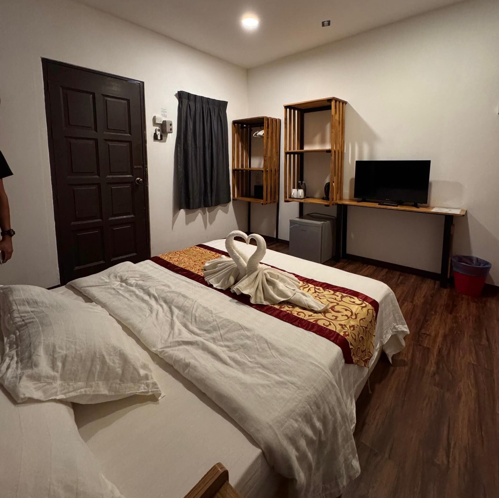 Habitación de hotel con cama, escritorio con televisor, refrigerador pequeño y basurero.