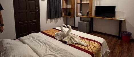 Habitación de hotel con cama, escritorio con televisor, refrigerador pequeño y basurero.