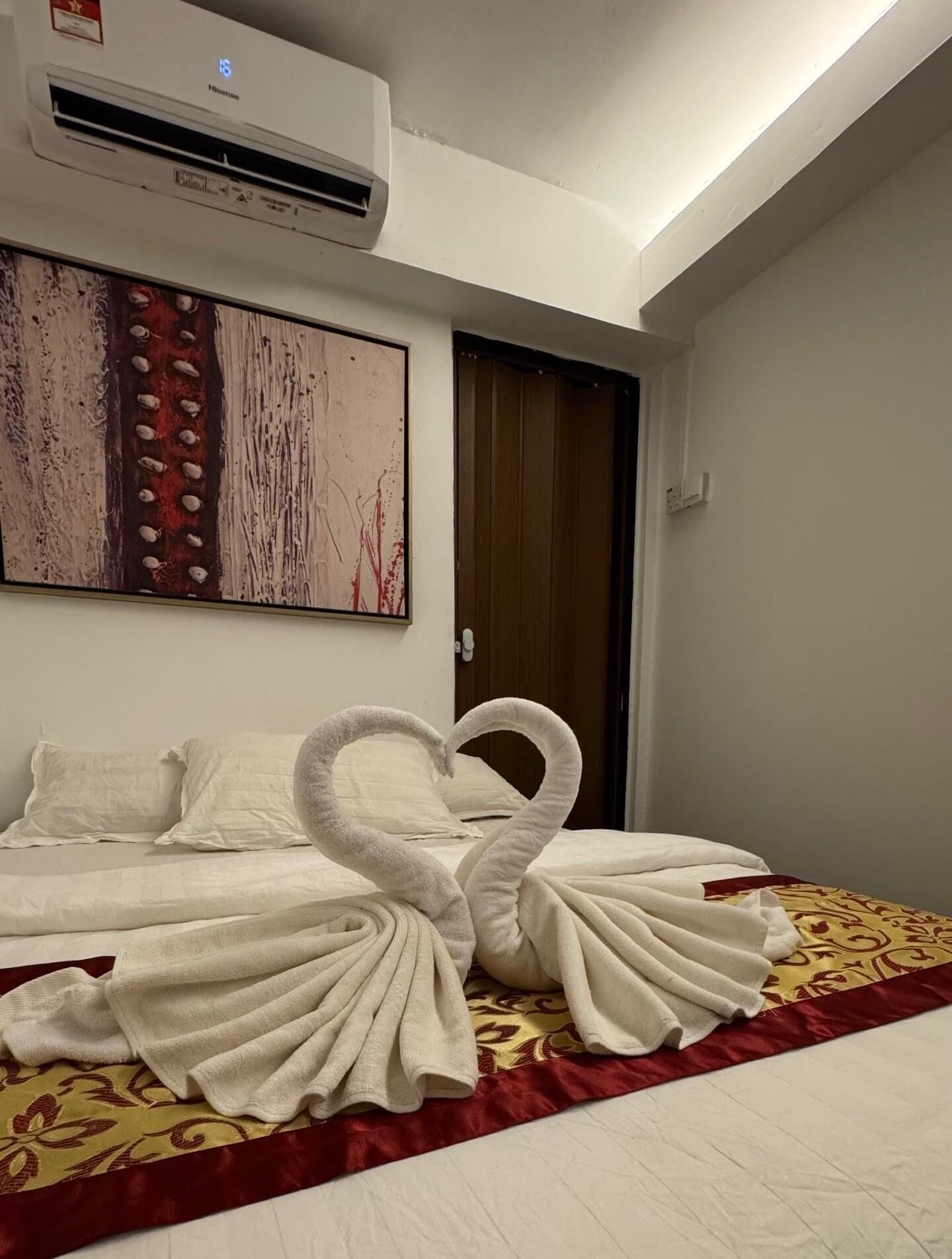 A hotel room with a bed, a wall-mounted air conditioner, and a painting.