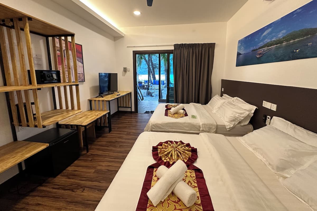 Une chambre d’hôtel avec deux lits, un bureau, une télévision et vue sur la plage.