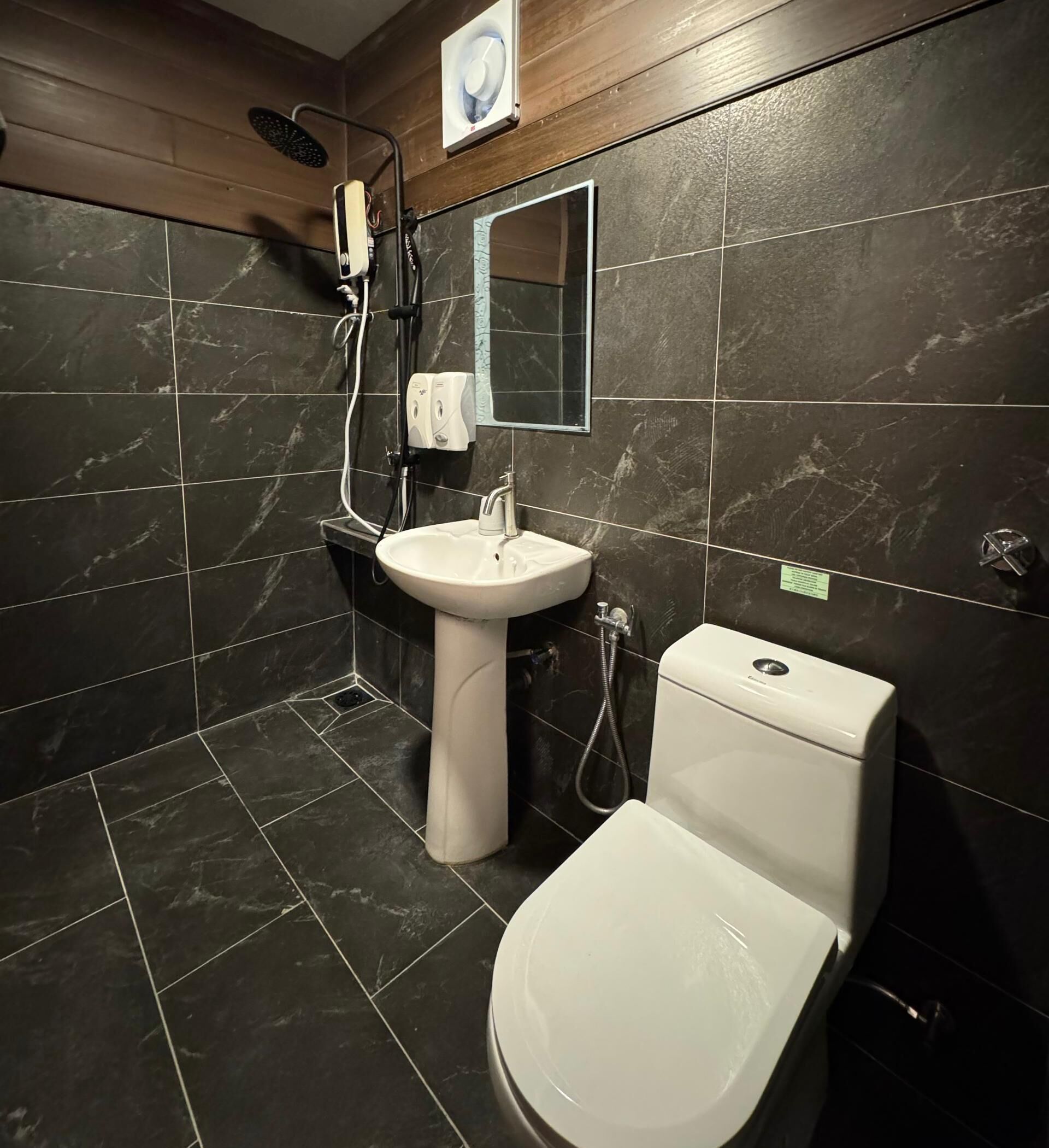 A modern bathroom with dark marble tiles, a white sink, a toilet, and a shower area.