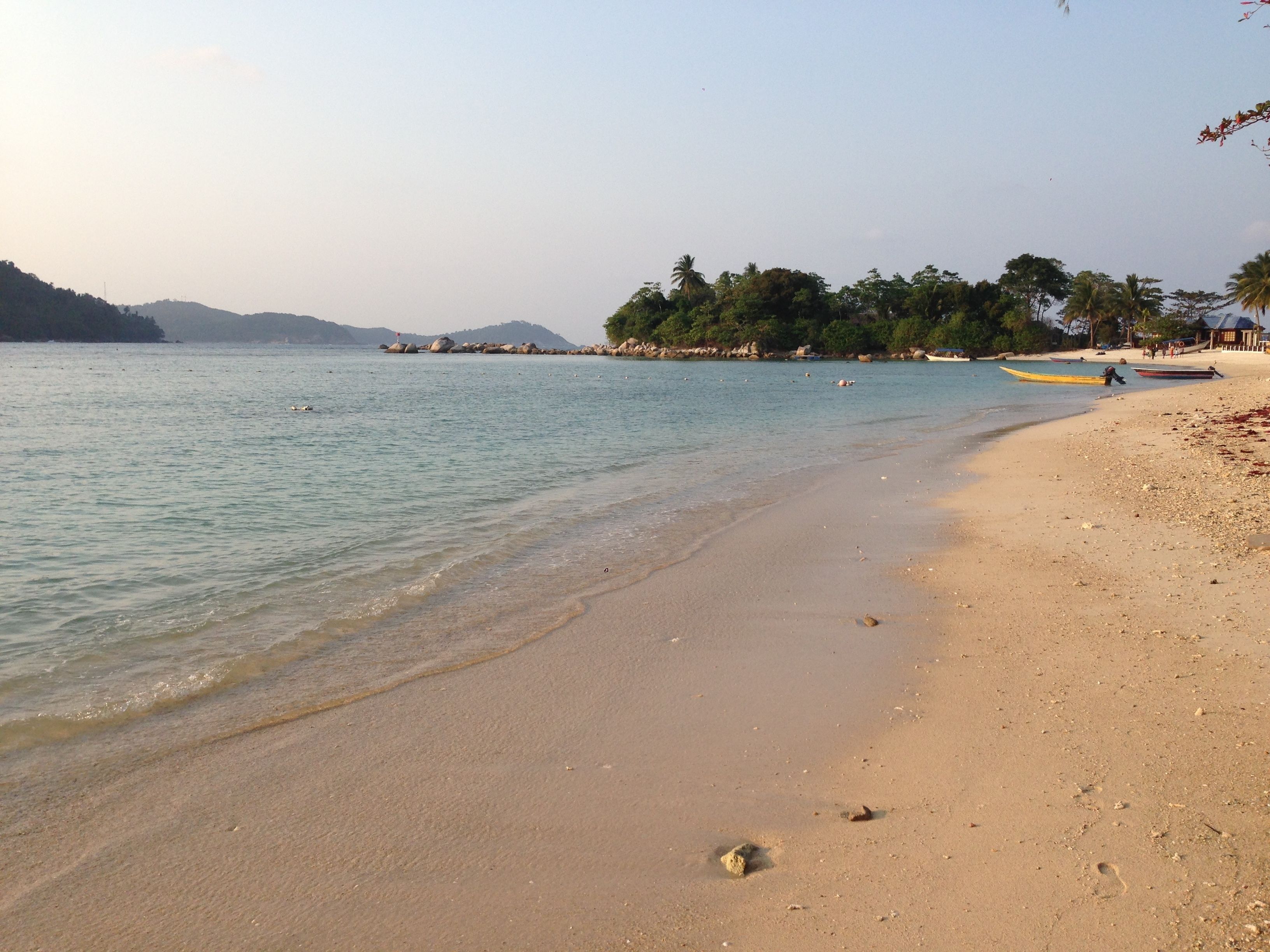 A beach with clear water, a sandy shore, and boats.