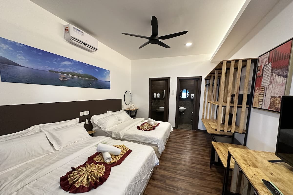 Une chambre d’hôtel avec deux lits, un ventilateur de plafond, un appareil de climatisation, un tableau représentant un paysage côtier, un banc en bois et un téléviseur.