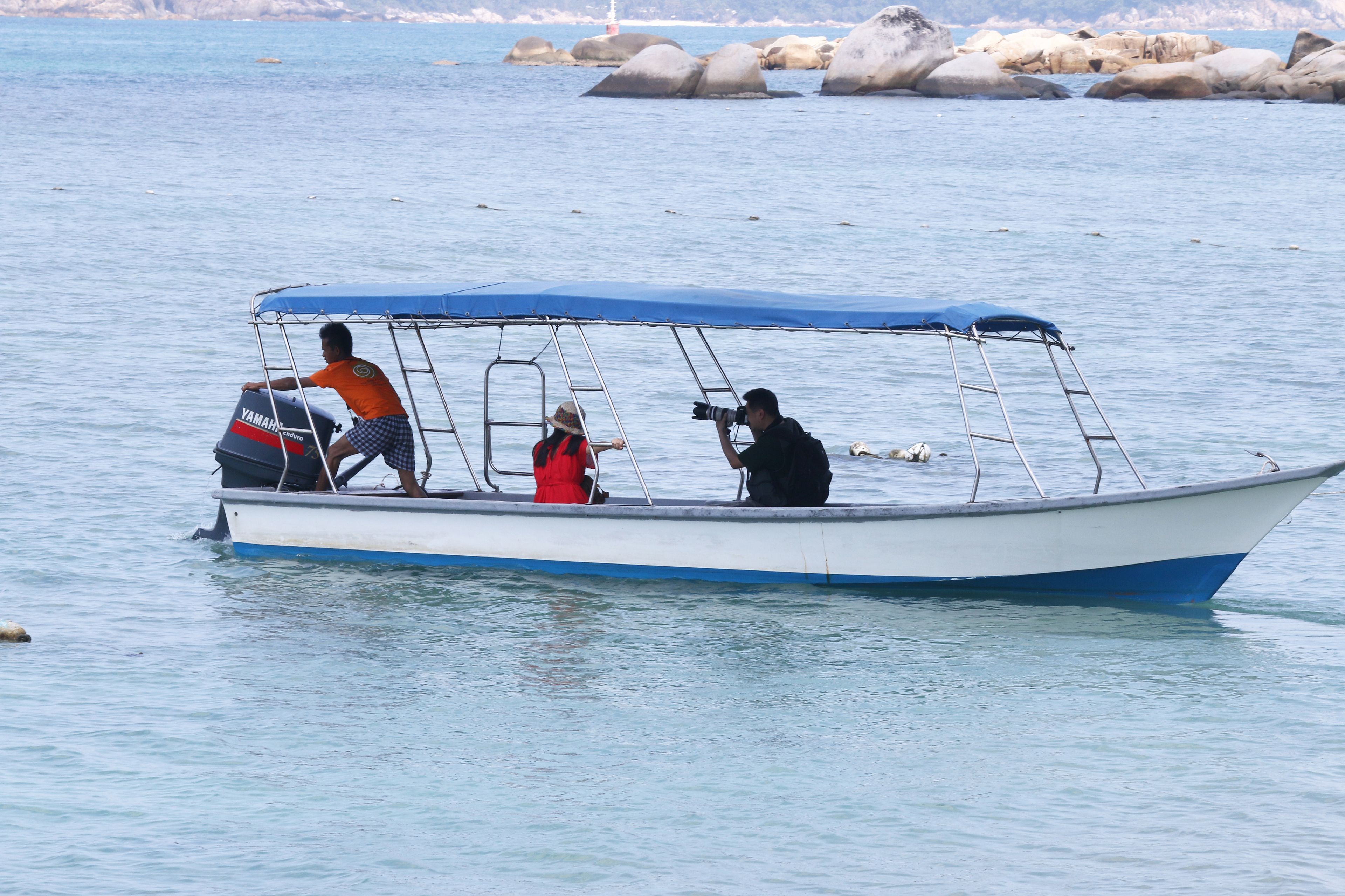 A small boat with a blue canopy, a Yamaha outboard motor, and three people on board.