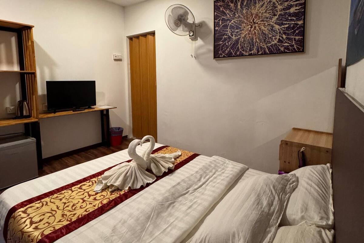 Une chambre d’hôtel équipée d’un lit, d’une télévision, d’un bureau et d’un ventilateur fixé au mur.