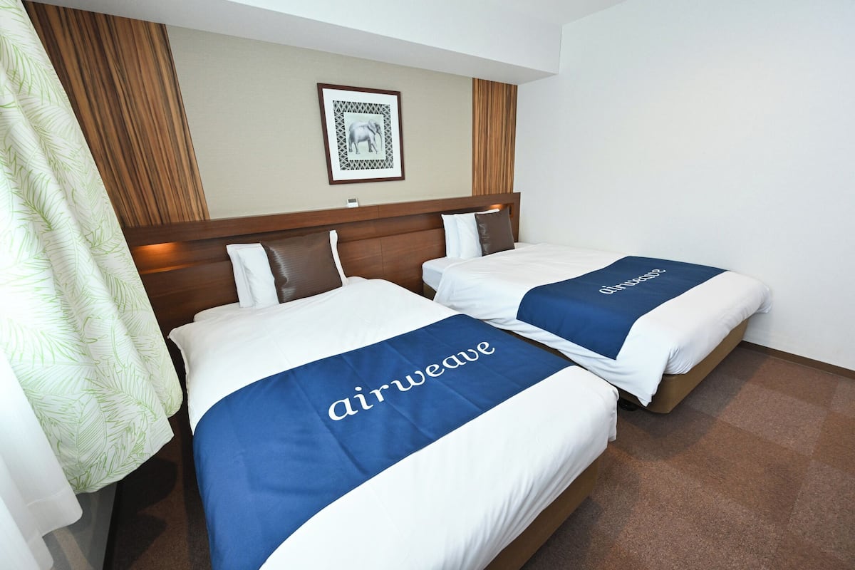 Two beds with 'airweave' branded bedspreads, a framed picture on the wall, and a wooden headboard.