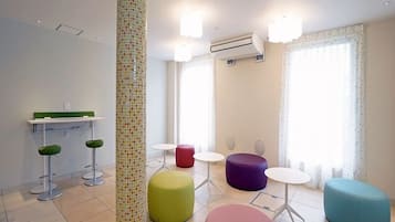 A modern, well-lit room with a tiled floor, a central pillar with mosaic tiles, a reception desk, and several colorful seating options.