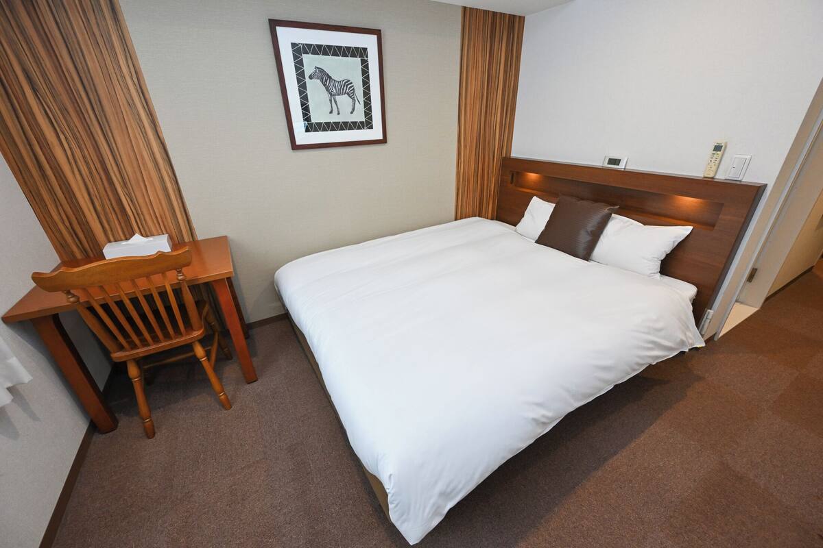 A hotel room with a bed, a desk, a chair, a framed picture on the wall, and a curtain.