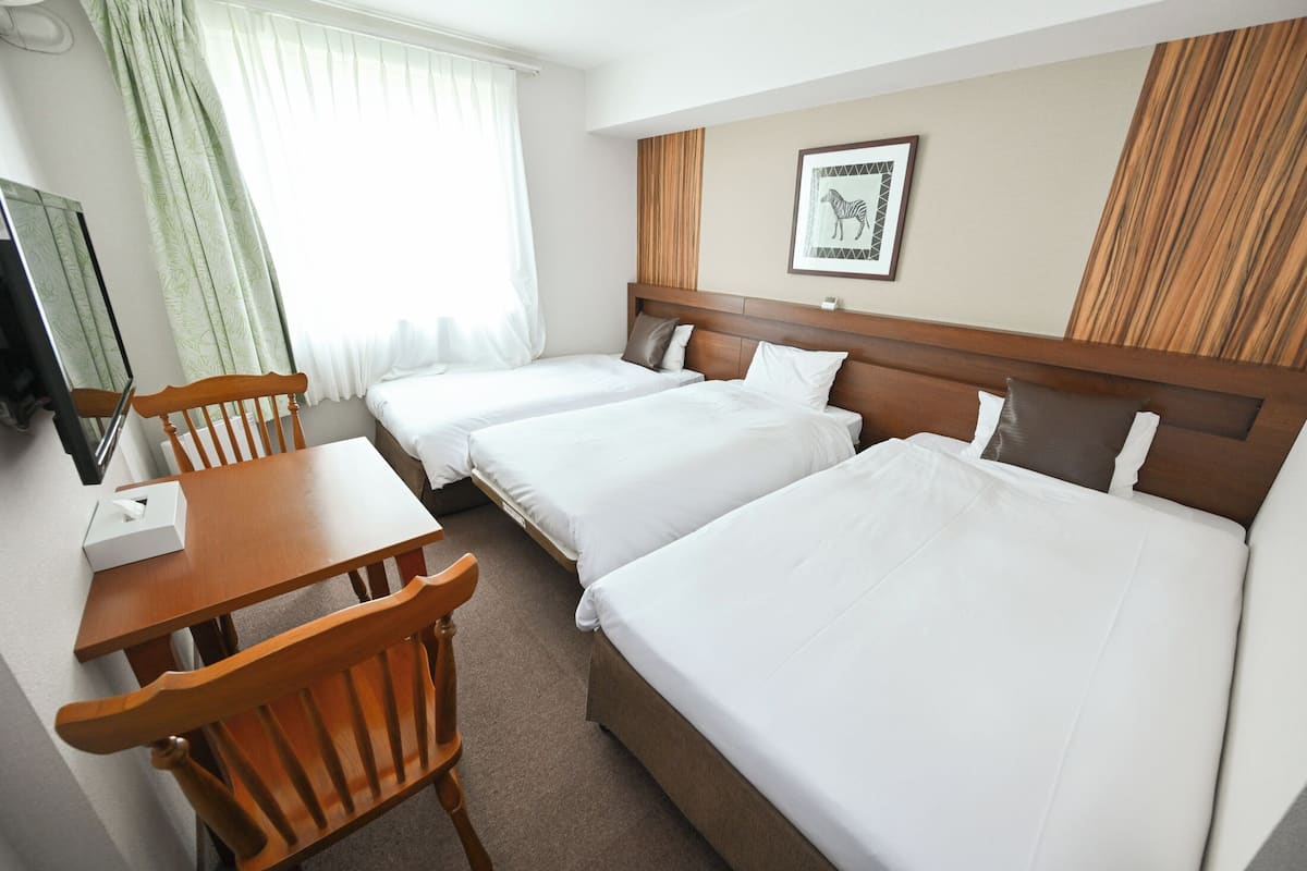 A hotel room with two beds, a wooden desk, a chair, a television, and a window with curtains.