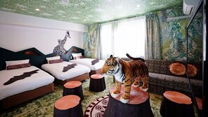 A room with a green leaf-patterned ceiling, a tiger statue on a wooden stool, a giraffe wall decal, and a patterned sofa. - La'gent Hotel Osaka Bay (Osaka)