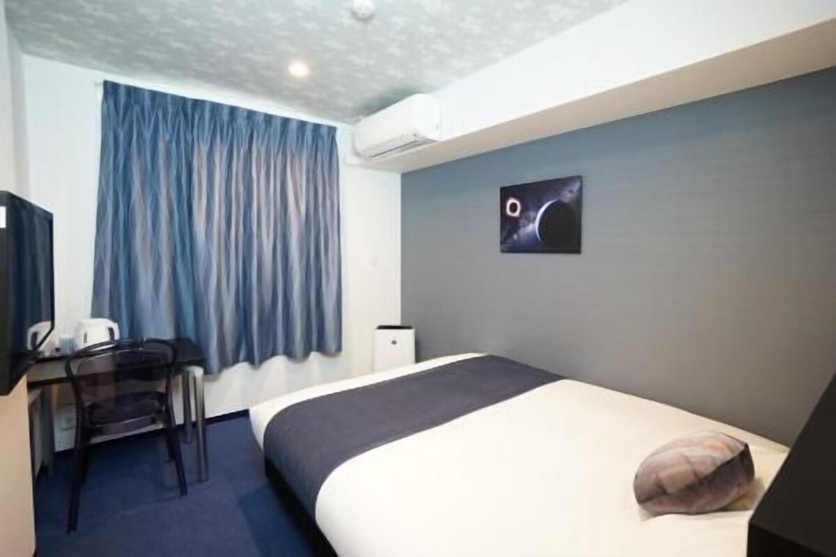 A hotel room with a bed, a desk, a chair, a television, and a wall-mounted artwork.