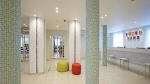 A spacious lobby with tiled floors, a reception desk, and a seating area with colorful stools. - La'gent Hotel Osaka Bay (Osaka)