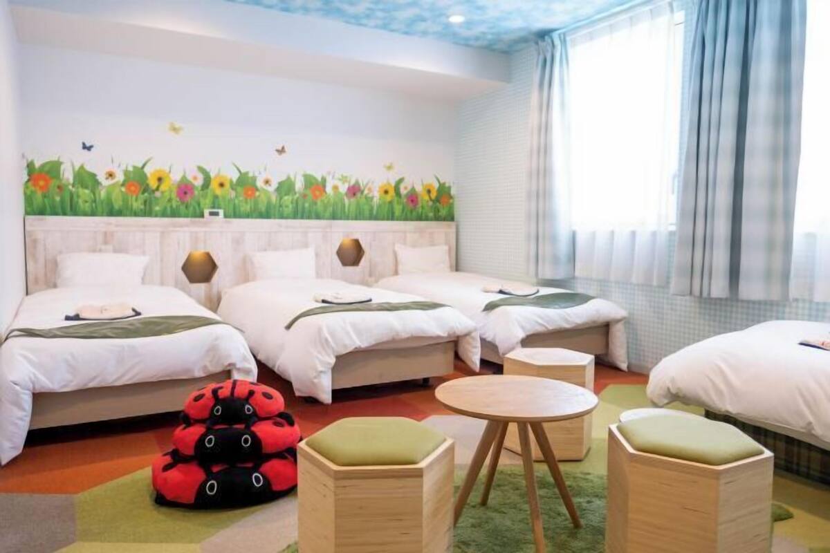 A hotel room with three beds, a round table, and a wall mural.
