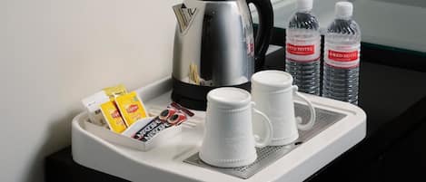 A tray with a coffee maker, two water bottles, a coffee pod, a packet of creamer, and two white mugs.