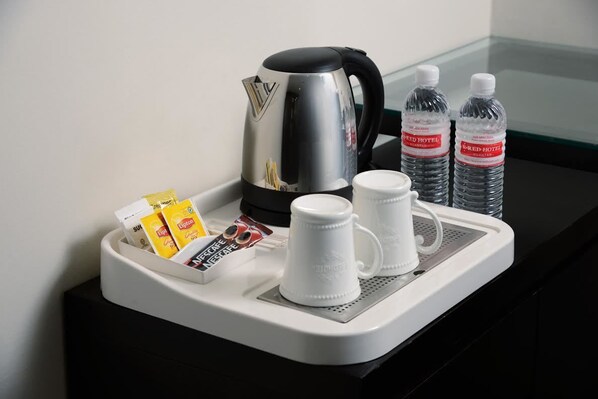 A tray with a coffee maker, two water bottles, a coffee pod, a packet of creamer, and two white mugs. - E-Red Hotel Sdn Bhd (Kuantan)