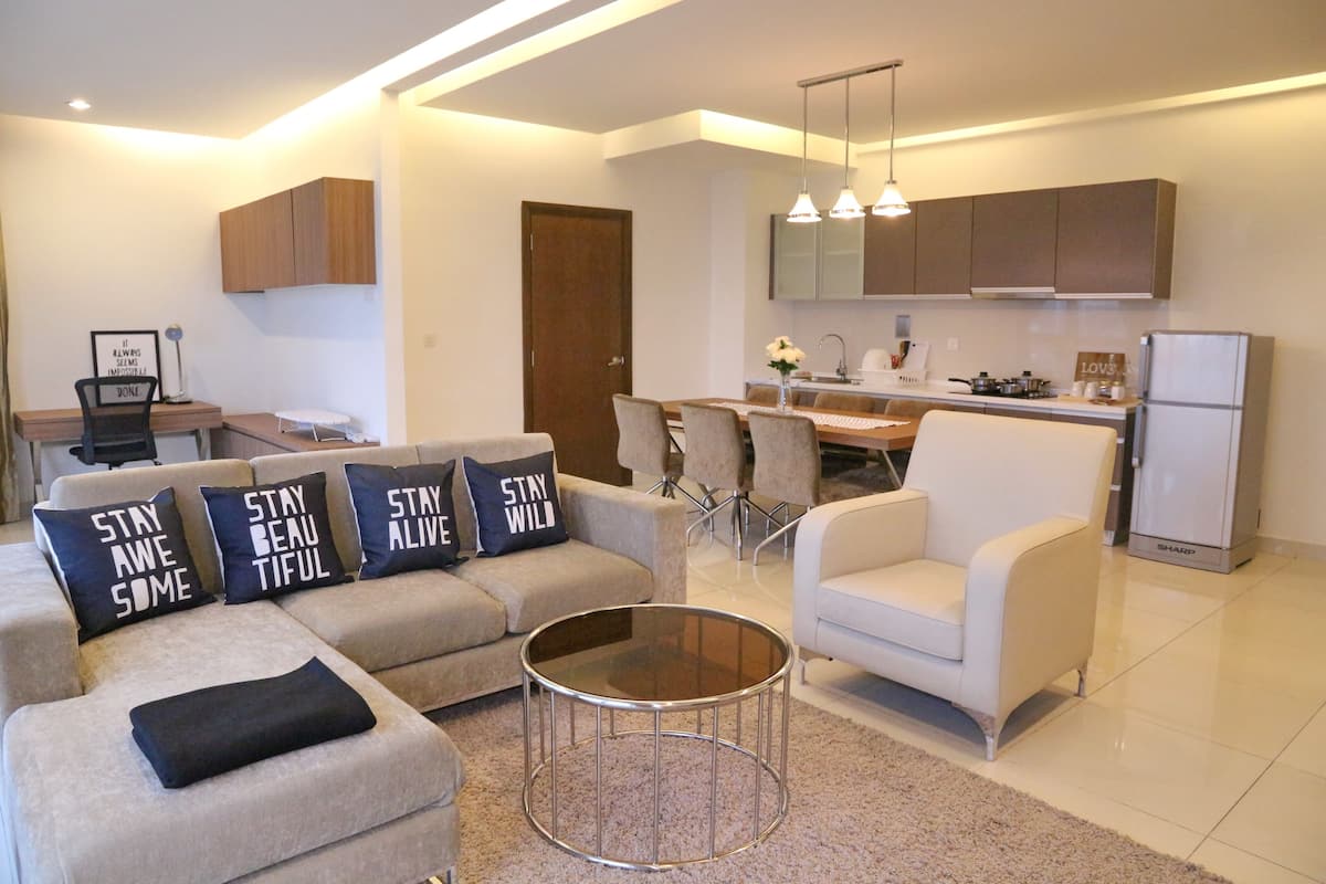 A modern living room with a sofa, armchairs, and a coffee table. There is a dining area with a table and chairs, and a kitchen with cabinets and appliances.