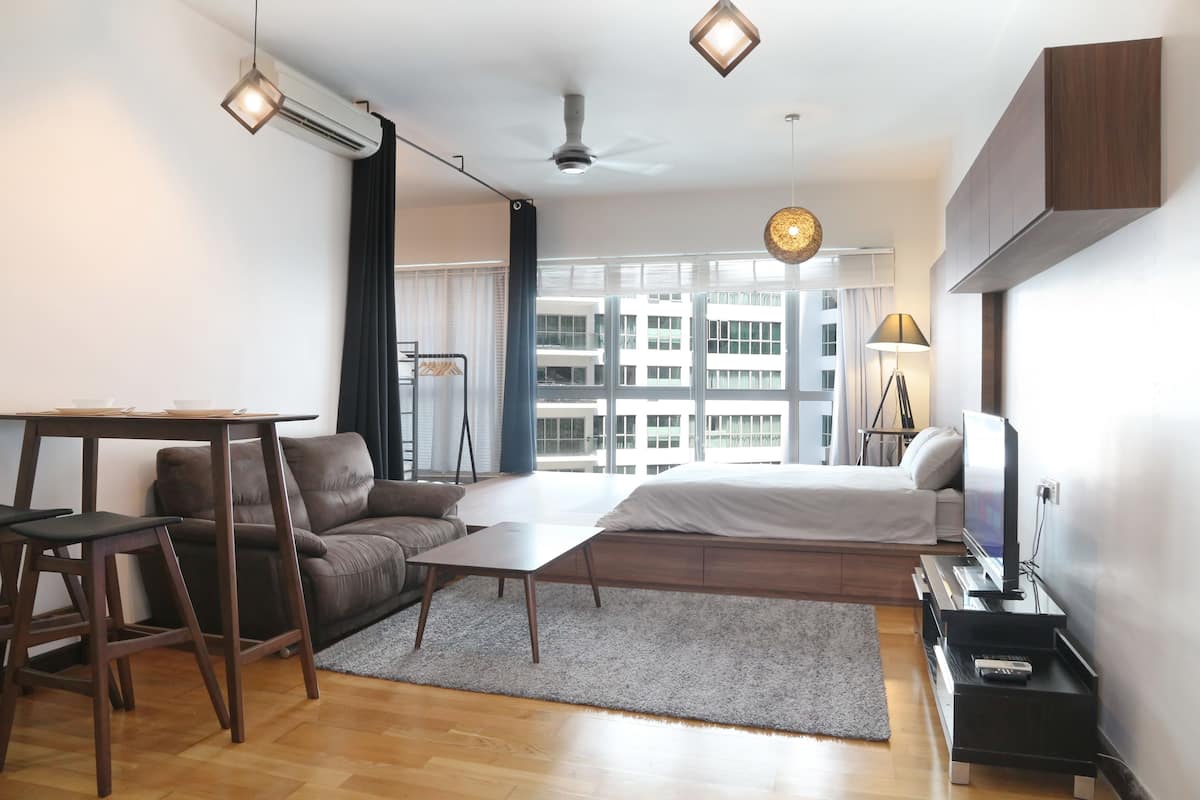 A modern bedroom with a bed, a desk, a sofa, and a TV.