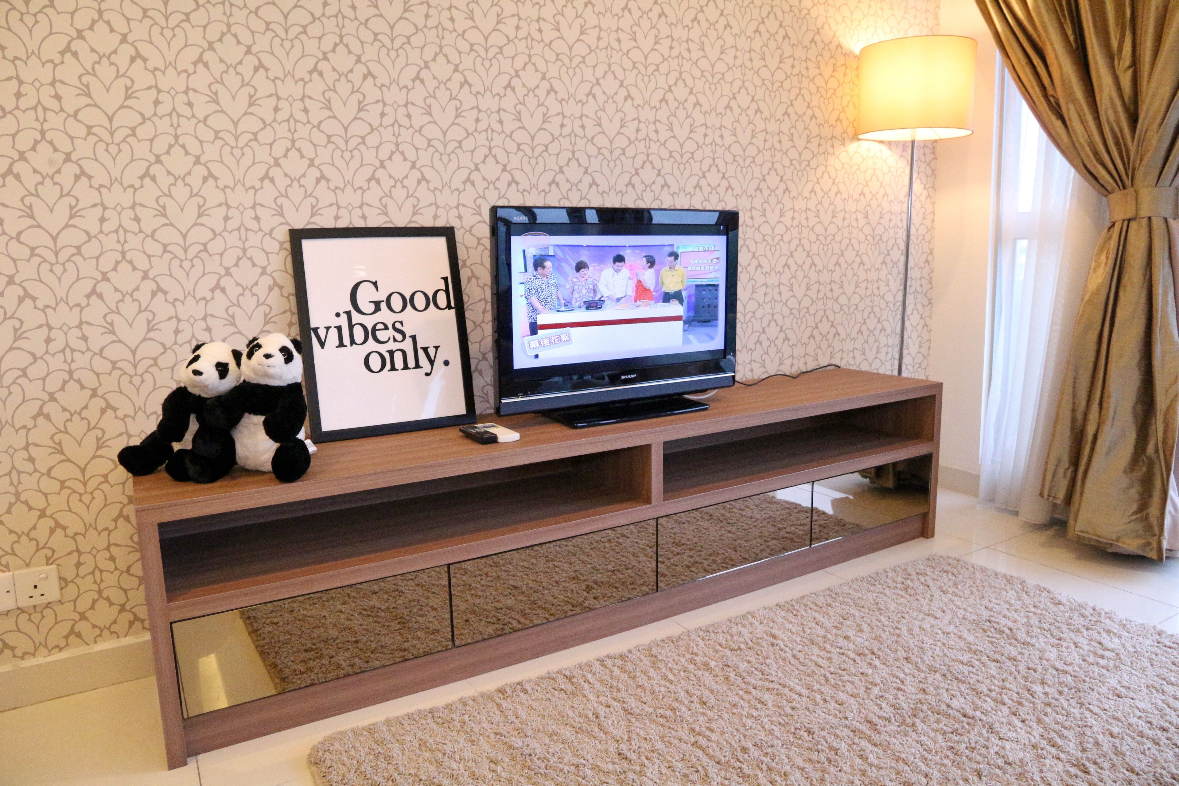 A TV on a wooden stand with a framed sign saying "Good vibes only." and two stuffed pandas.