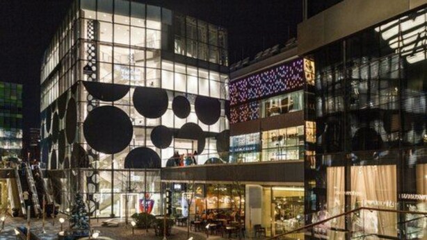 Un bâtiment moderne doté d’une façade en verre et d’ouvertures circulaires, comprenant un café au rez-de-chaussée et des espaces commerciaux aux étages supérieurs.