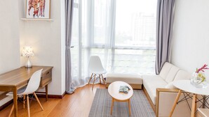 Une chambre d’hôtel moderne avec un bureau en bois, un canapé blanc et une grande fenêtre avec des rideaux.