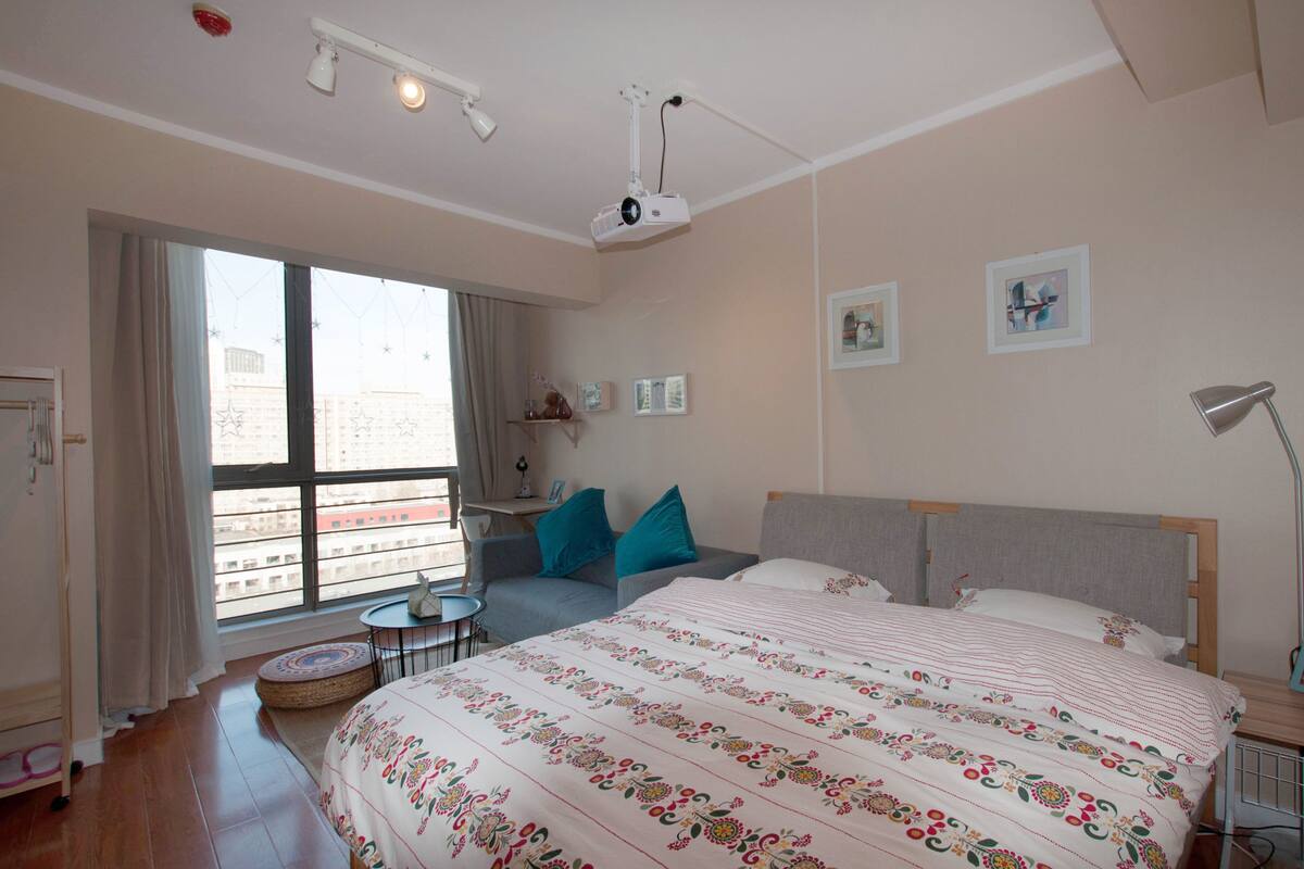 Una habitación de hotel con una cama grande, una mesita redonda pequeña, un sofá y un proyector montado en el techo.