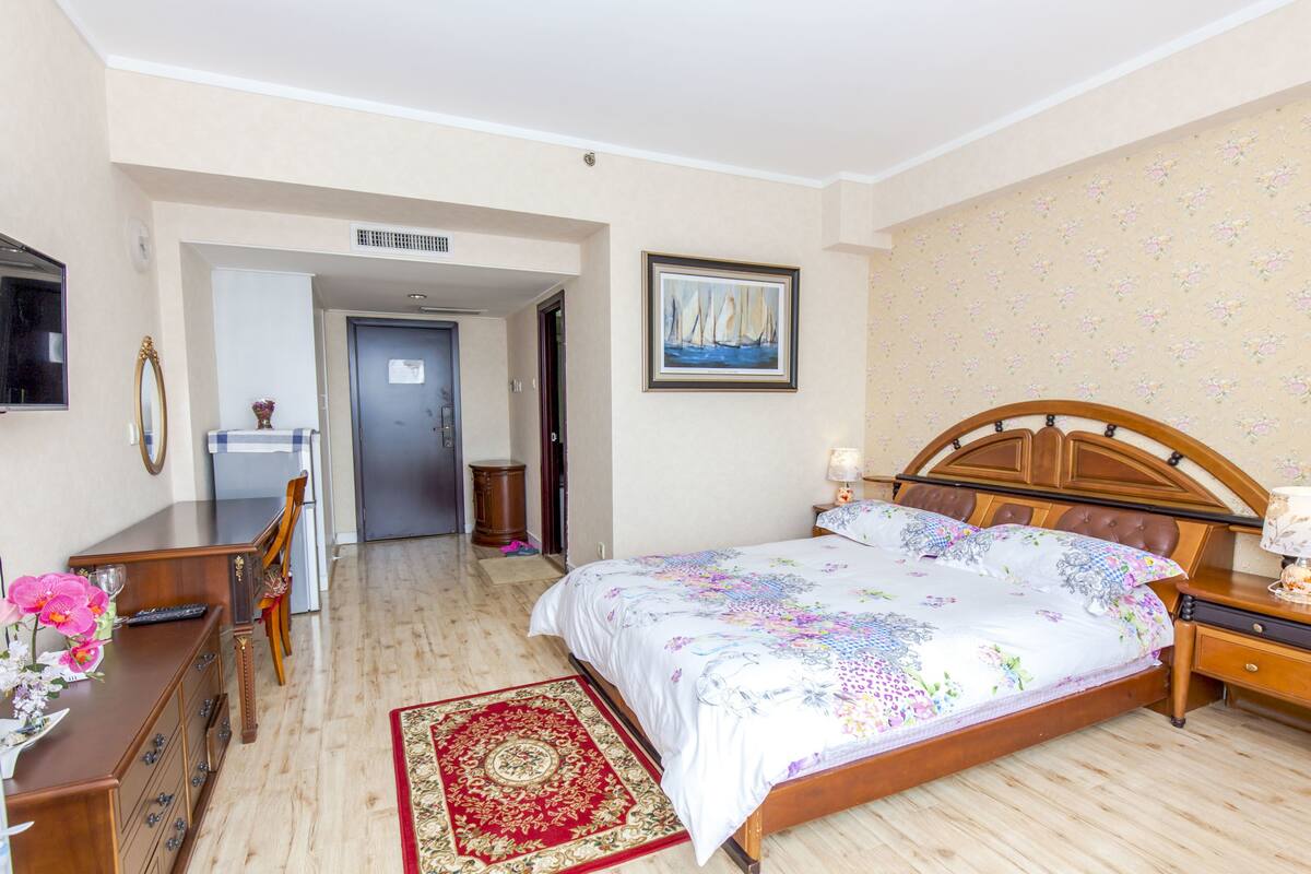 Un dormitorio con una cama de madera, un escritorio con silla, una alfombra roja y un cuadro en la pared.