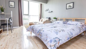 Une chambre moderne avec un grand lit, un bureau et une chaise. Il y a une fenêtre avec des rideaux, une plante et un tableau au mur.