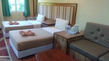A hotel room with two single beds, a sofa, a wooden nightstand, and a window with curtains.