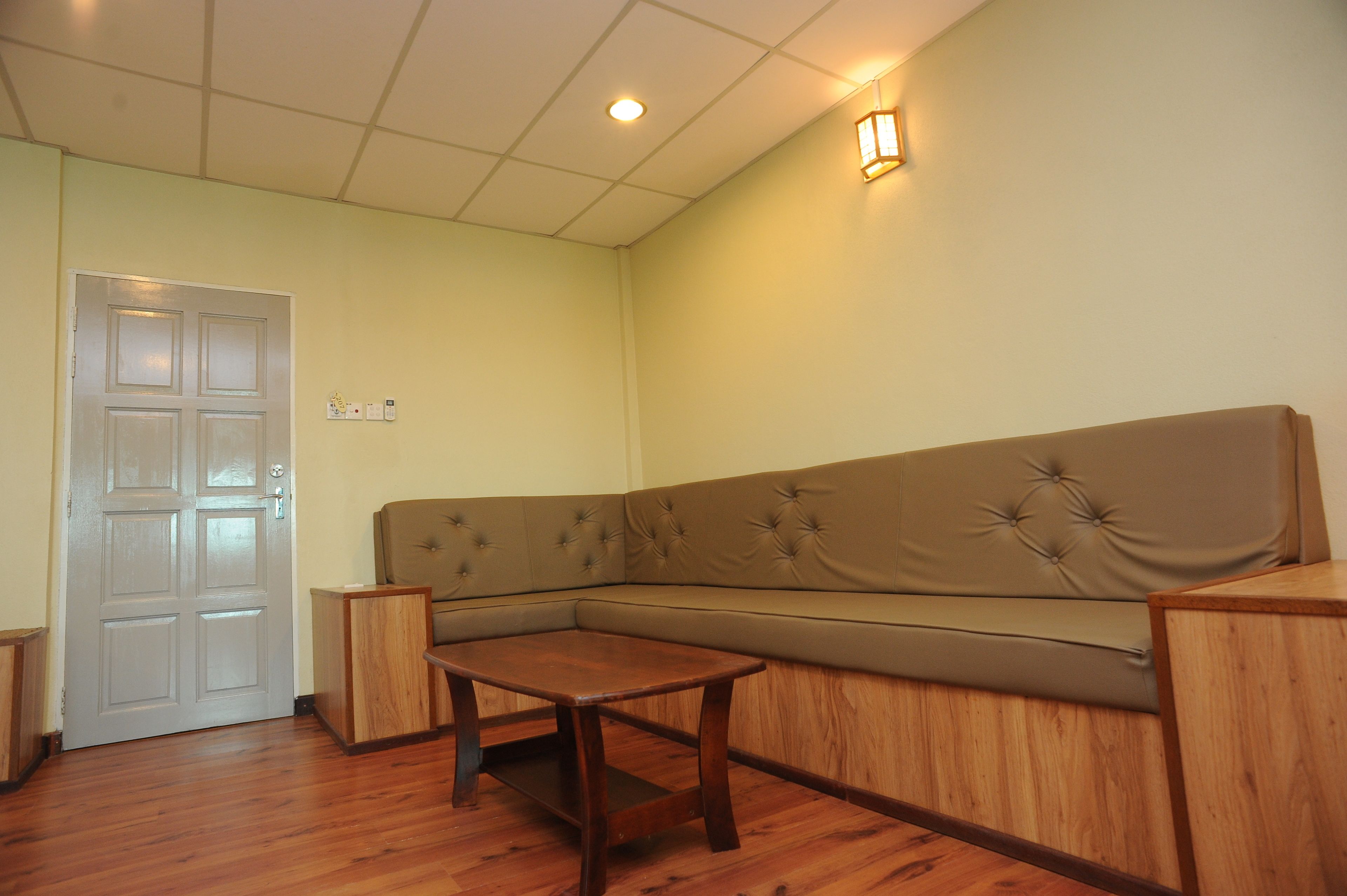 Una habitación con un sofá seccional color beige, una mesa de madera, una puerta blanca y una lámpara fijada a la pared.