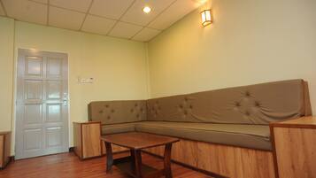 Una habitación con un sofá seccional color beige, una mesa de madera, una puerta blanca y una lámpara fijada a la pared.