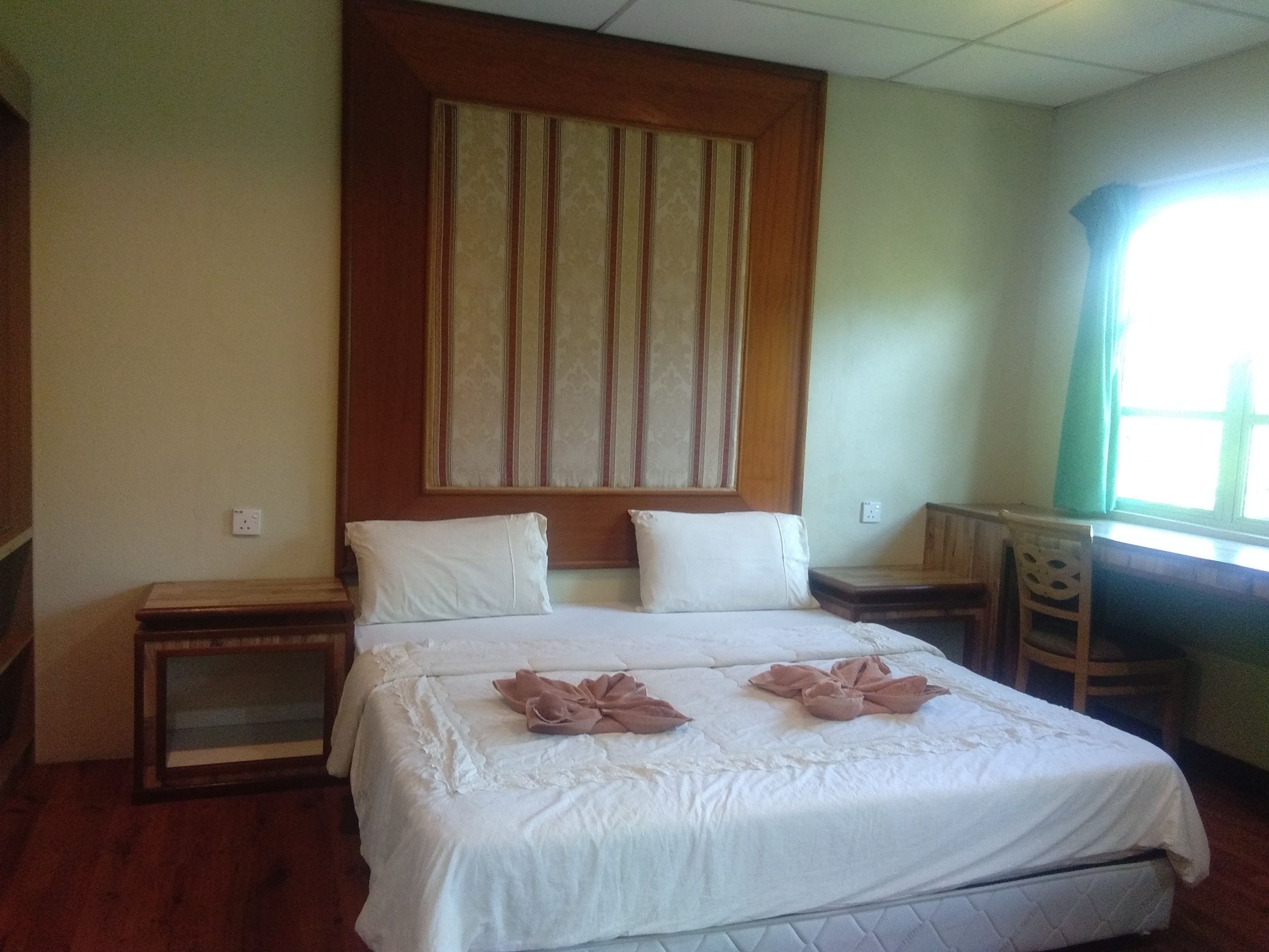 A hotel room with a large bed, two bedside tables, a window with curtains, and a wall-mounted artwork.
