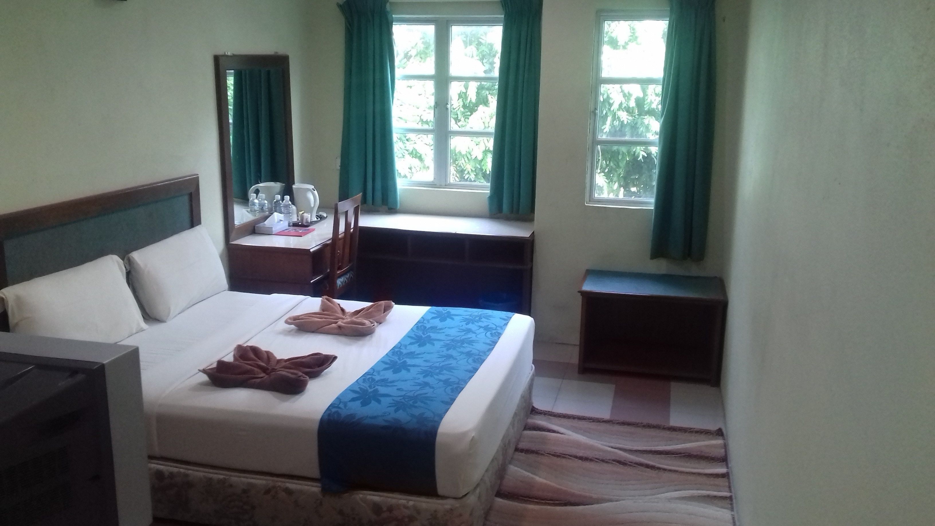 A hotel room with a bed, a desk, and a window with curtains.