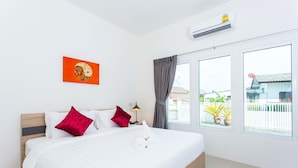 A hotel room with a bed, a window with curtains, a wall-mounted air conditioner, and a small table with a lamp. - The Way Phuket Resort (Thep Krasattri)