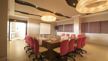 A conference room with a long table, red chairs, a projector screen, and a modern ceiling design.