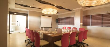 A conference room with a long table, red chairs, a projector screen, and a modern ceiling design.