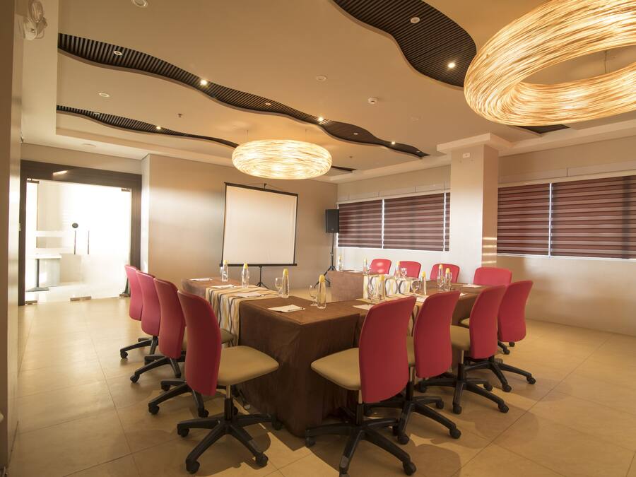 A conference room with a long table, red chairs, a projector screen, and a modern ceiling design.