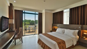 A modern hotel room with a large bed, a desk with a television, and a balcony with a view of greenery. - Kew Hotel (Tagbilaran)