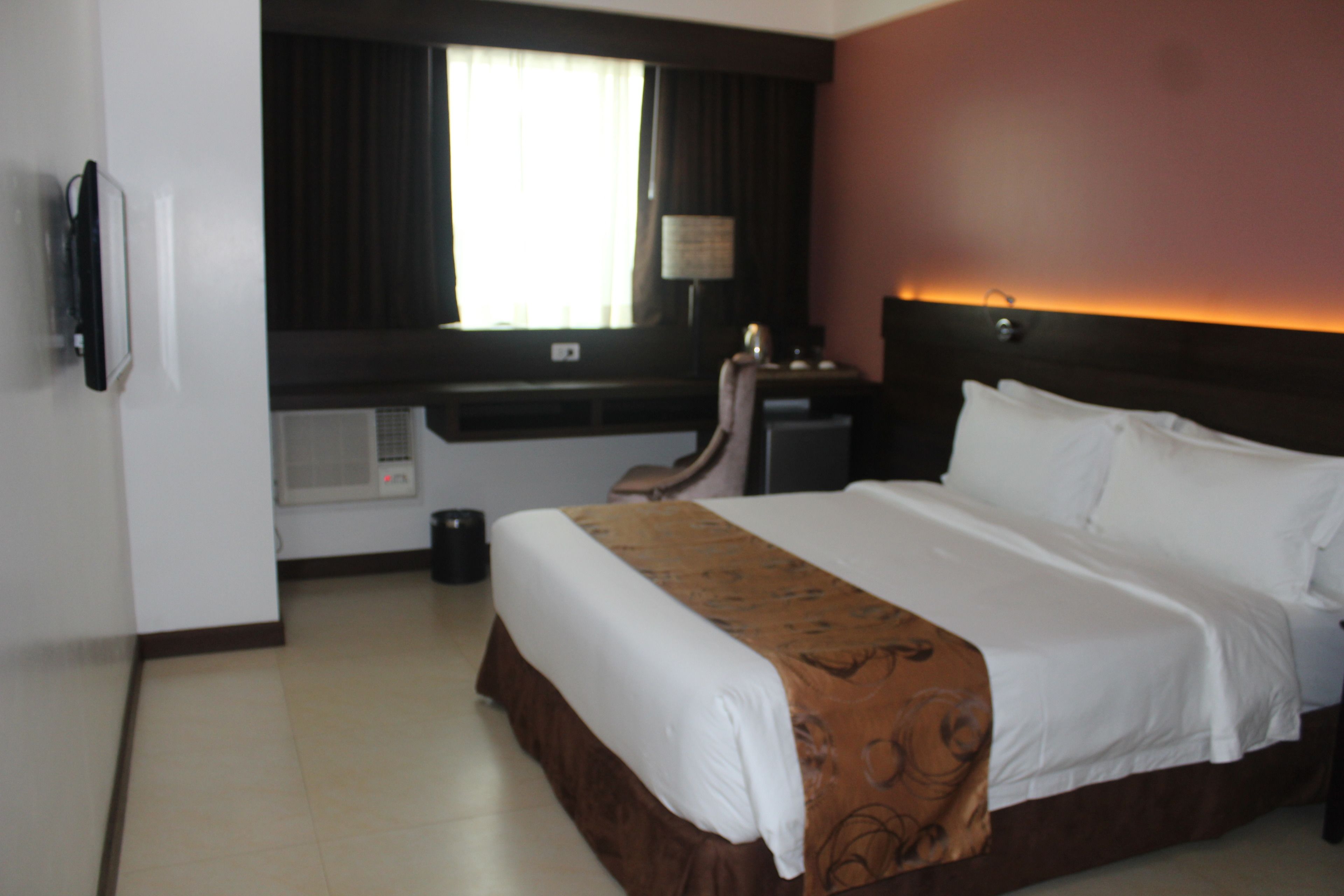 A hotel room with a large bed, a desk, and a window with curtains.