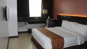 A hotel room with a large bed, a desk, and a window with curtains.