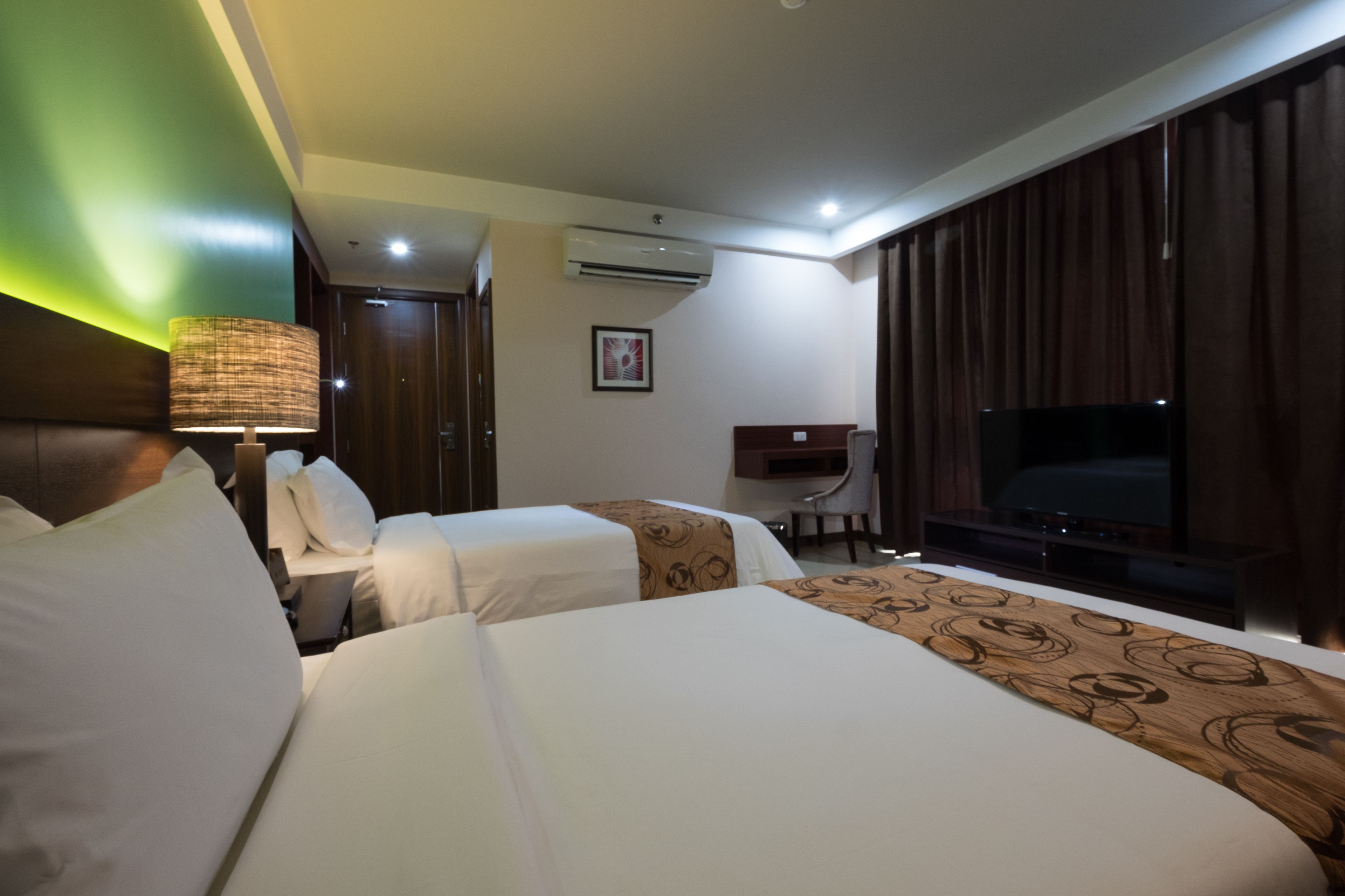 Une chambre d’hôtel avec deux lits, un bureau, une chaise, une télévision et un appareil de climatisation.