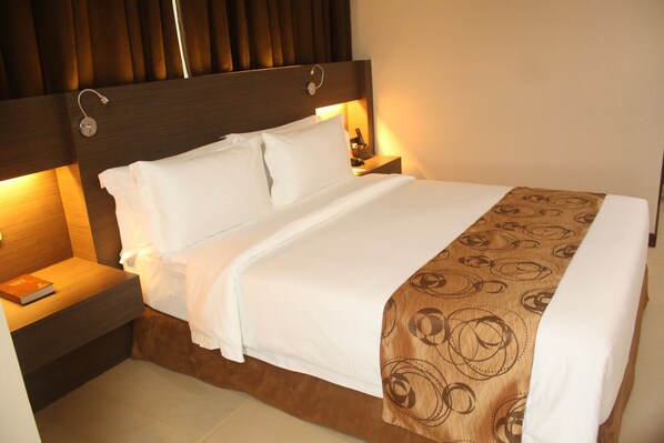 A neatly made bed with a patterned throw, a bedside table with a book, and a wall-mounted light fixture.