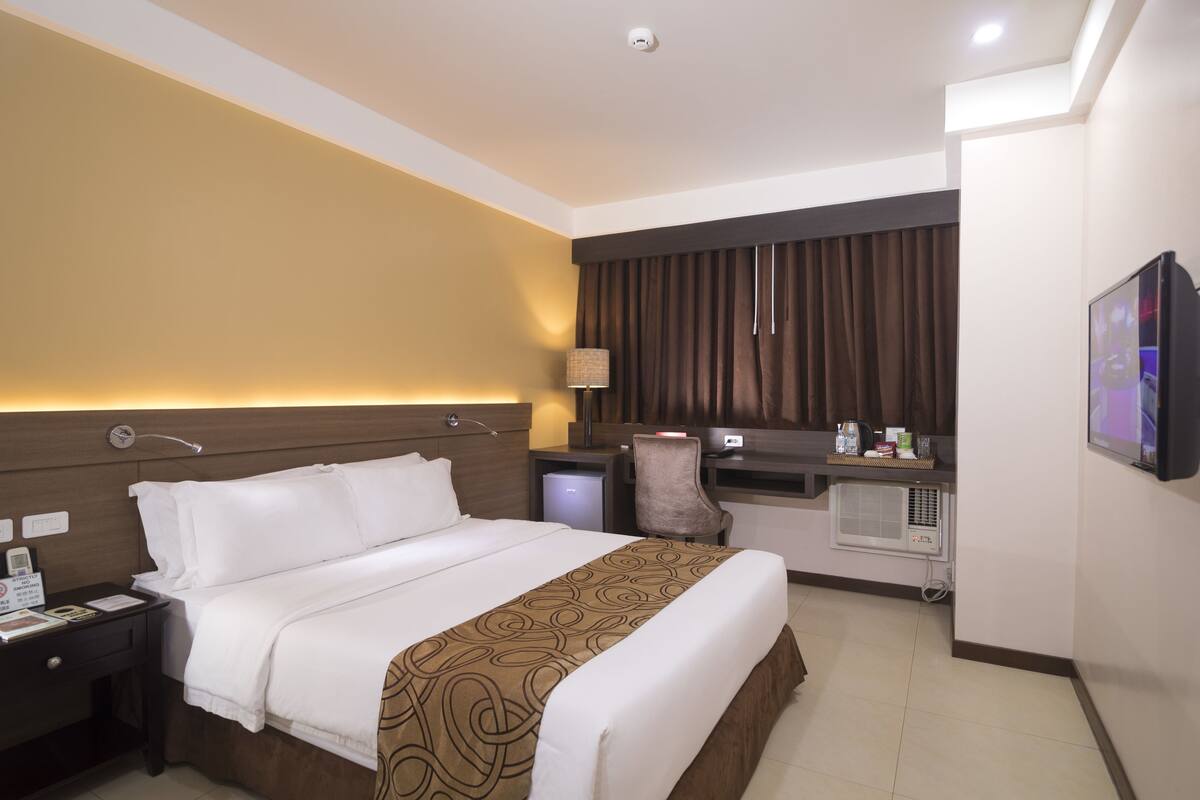 Ein Hotelzimmer mit Bett, Schreibtisch, Stuhl, Fernseher und Minibar.